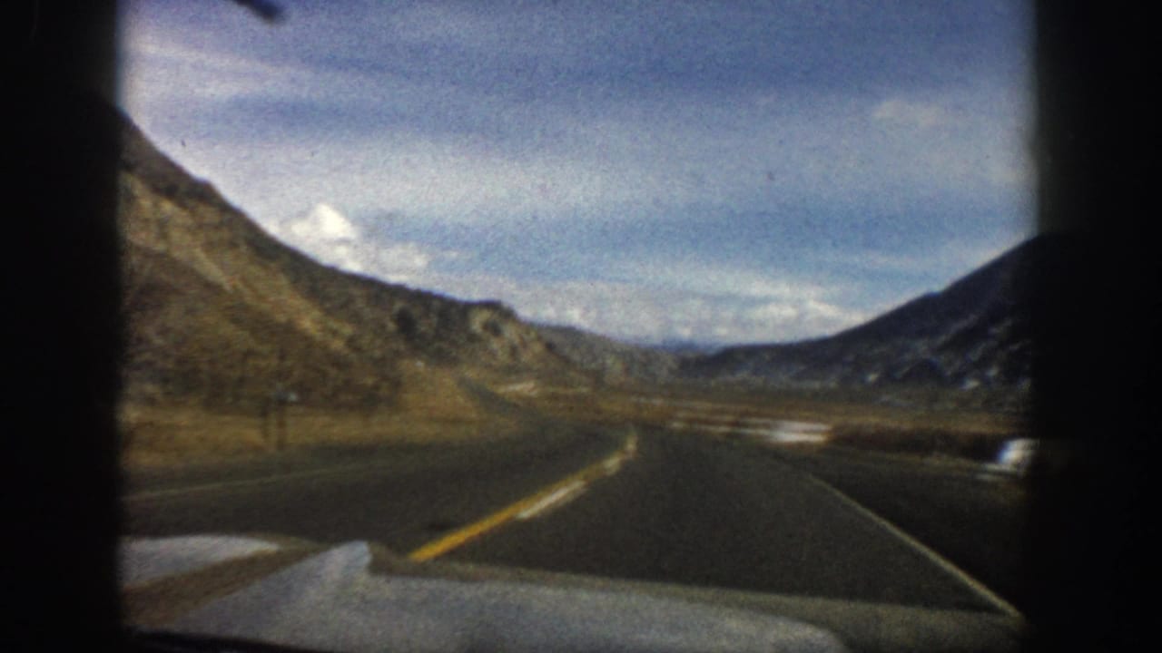 Curving highway through a mountain valley with the car hood visible at the bottom.