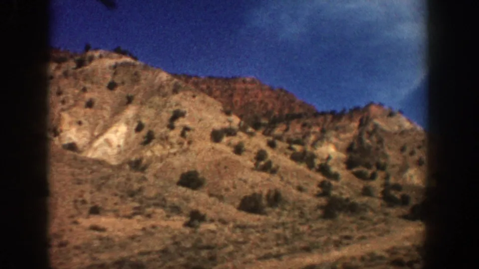 1961 Colorado mountain travel footage shifts to a closer view of a rocky, sparsely vegetated hillside under blue sky.