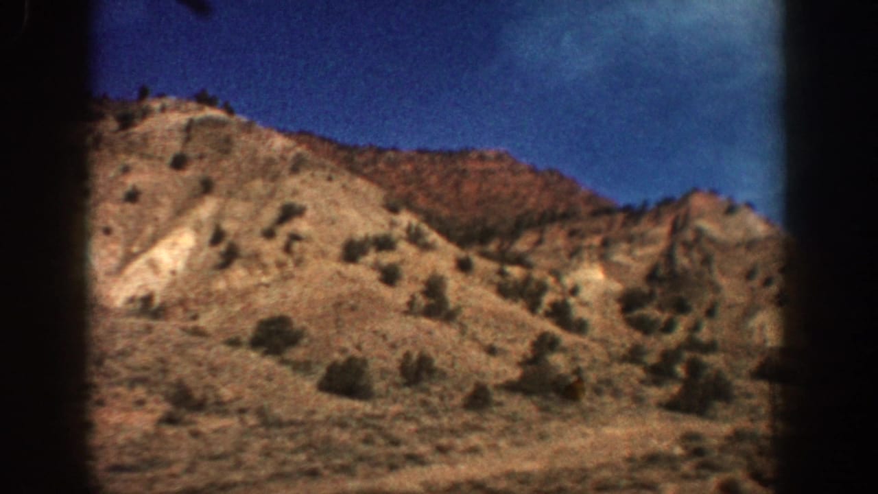 1961 Aspen, Colorado home-movie frame of a dry shrub-dotted hillside seen from a moving vantage under a bright blue sky.