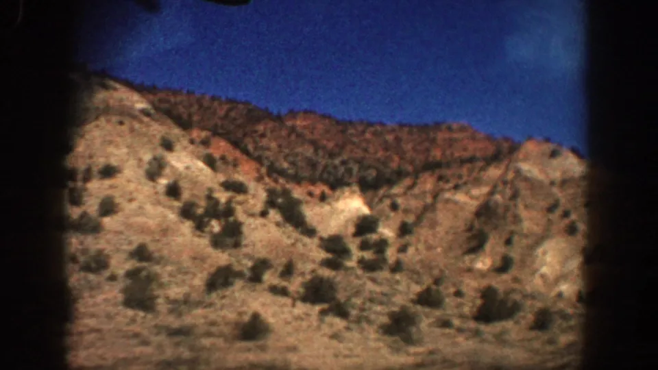 1961 Aspen, Colorado home-movie still of scrubby hills and a pale eroded section, softened by motion and 8mm grain.