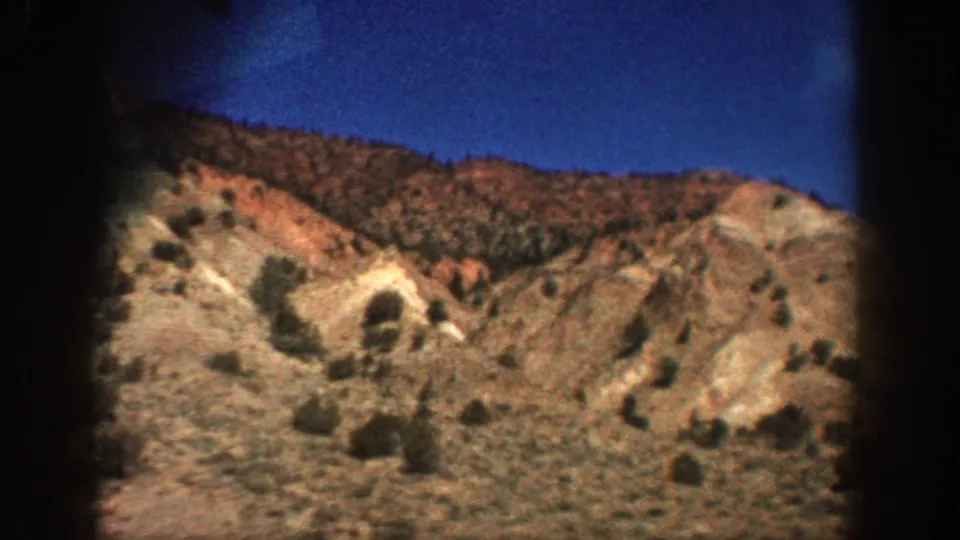 1961 Aspen, Colorado frame of dry hillsides with scattered shrubs and pale exposed earth, viewed through dark 8mm frame borders.