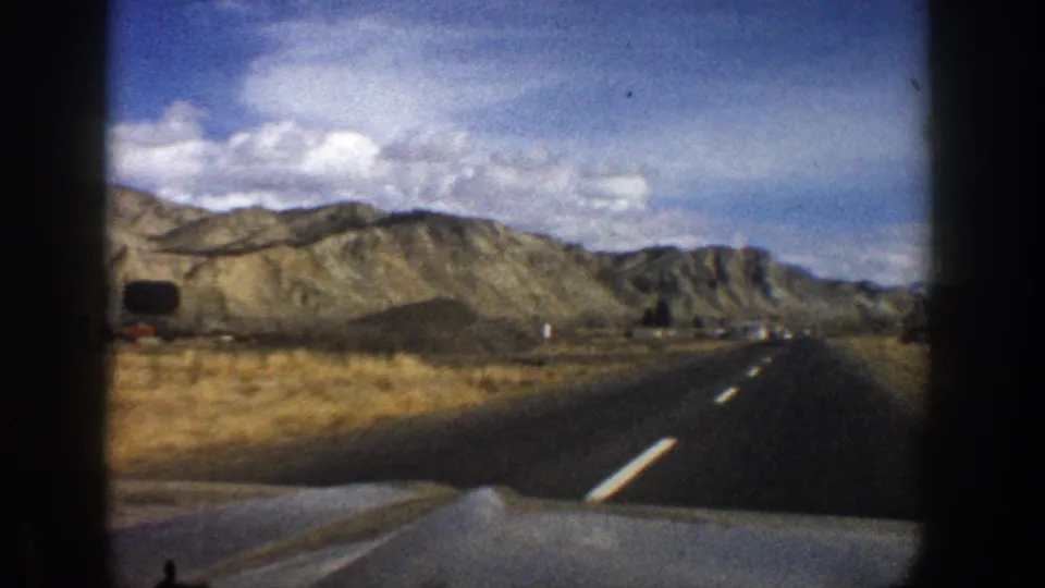 1961 Aspen, Colorado home-movie view of an open highway stretching toward dry mountain terrain, filmed from inside a moving car.