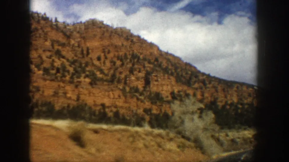 Passenger-window view of Aspen-area mountain terrain in 1961, with motion-blurred road edge and dry vegetation.
