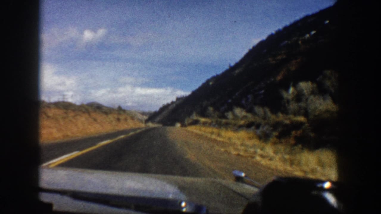 Forward 8mm car view on a winding Aspen, Colorado mountain road with scrub, slope, and open sky.