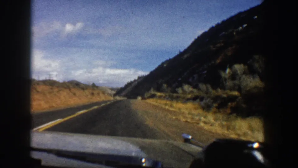 Forward 8mm car view on a winding Aspen, Colorado mountain road with scrub, slope, and open sky.
