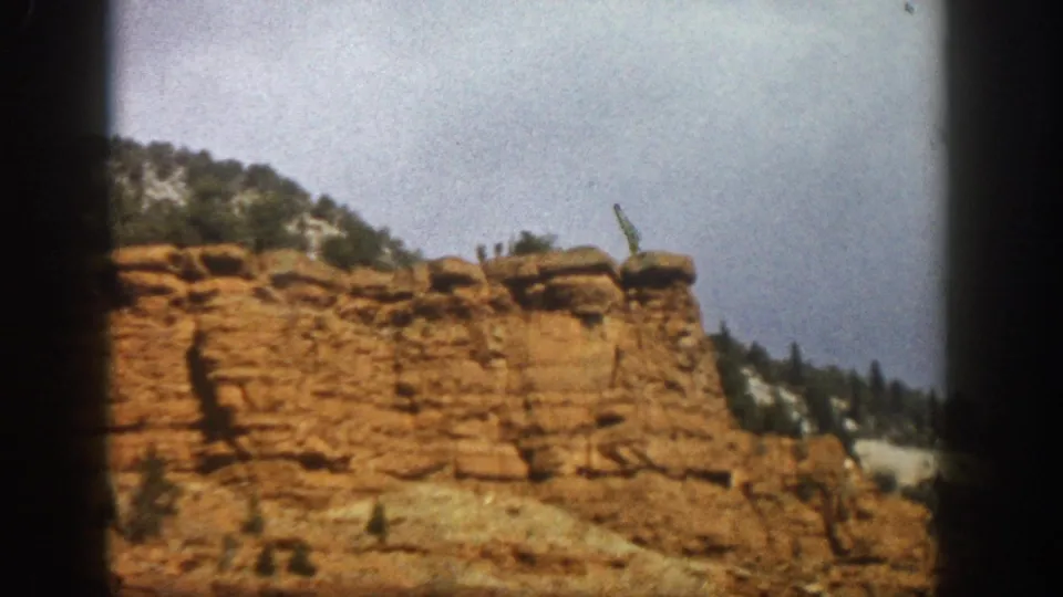 1961 8mm frame of a reddish rock outcrop near Aspen, Colorado, with sparse vegetation and sky beyond.