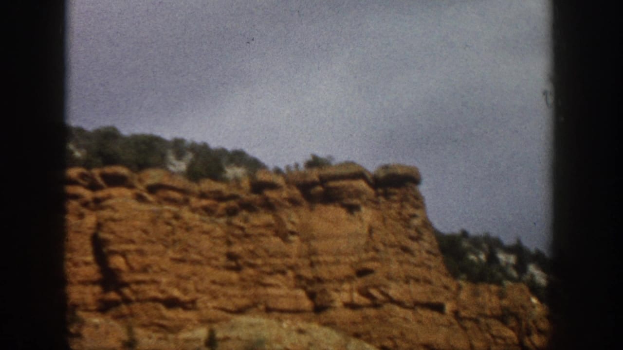 Red rock formation with trees along the top under a muted sky.