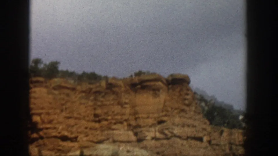 Final 1961 Aspen, Colorado frame showing a soft, slightly blurred red rock ridge with trees above and an overcast sky.