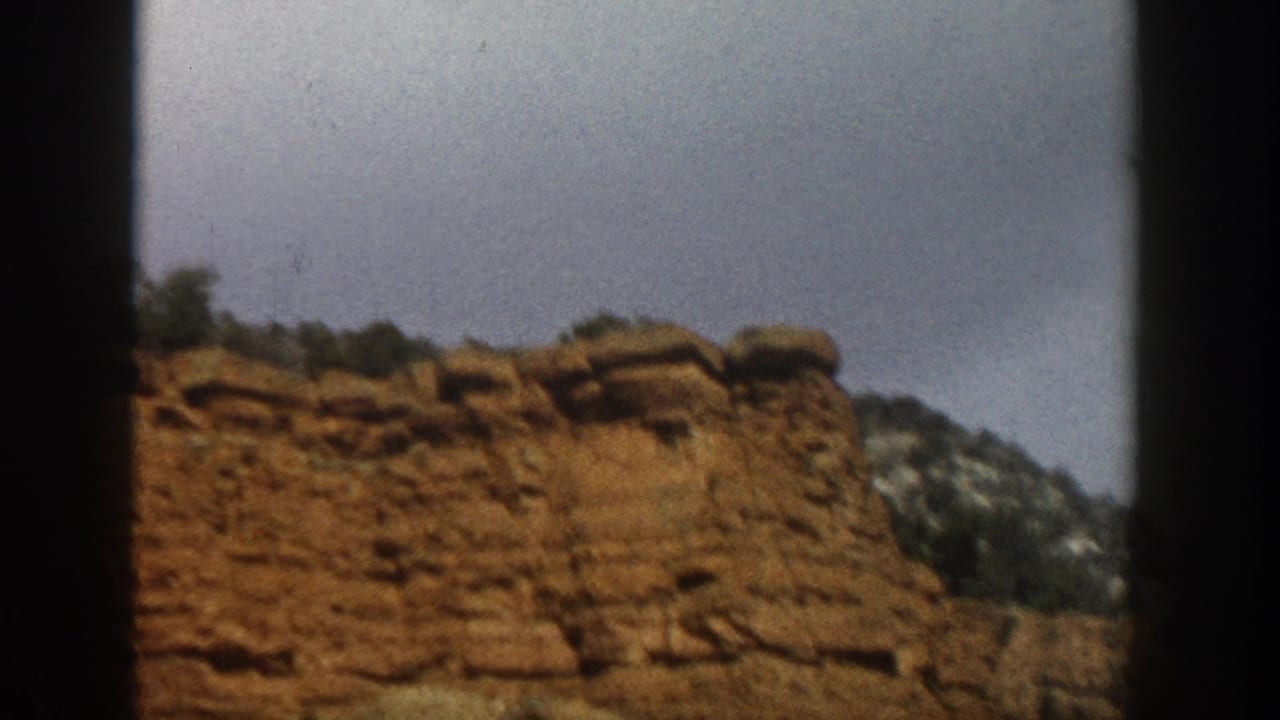 1961 Aspen, Colorado travel footage showing red rock cliffs and scrubland seen through a dark vehicle-window frame.