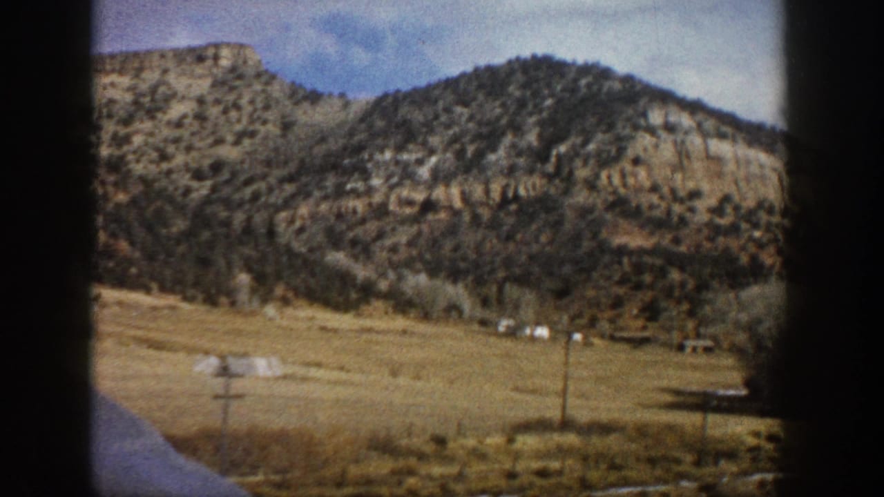 Dry field, utility poles, and shrub-covered mountains seen from a vehicle window.