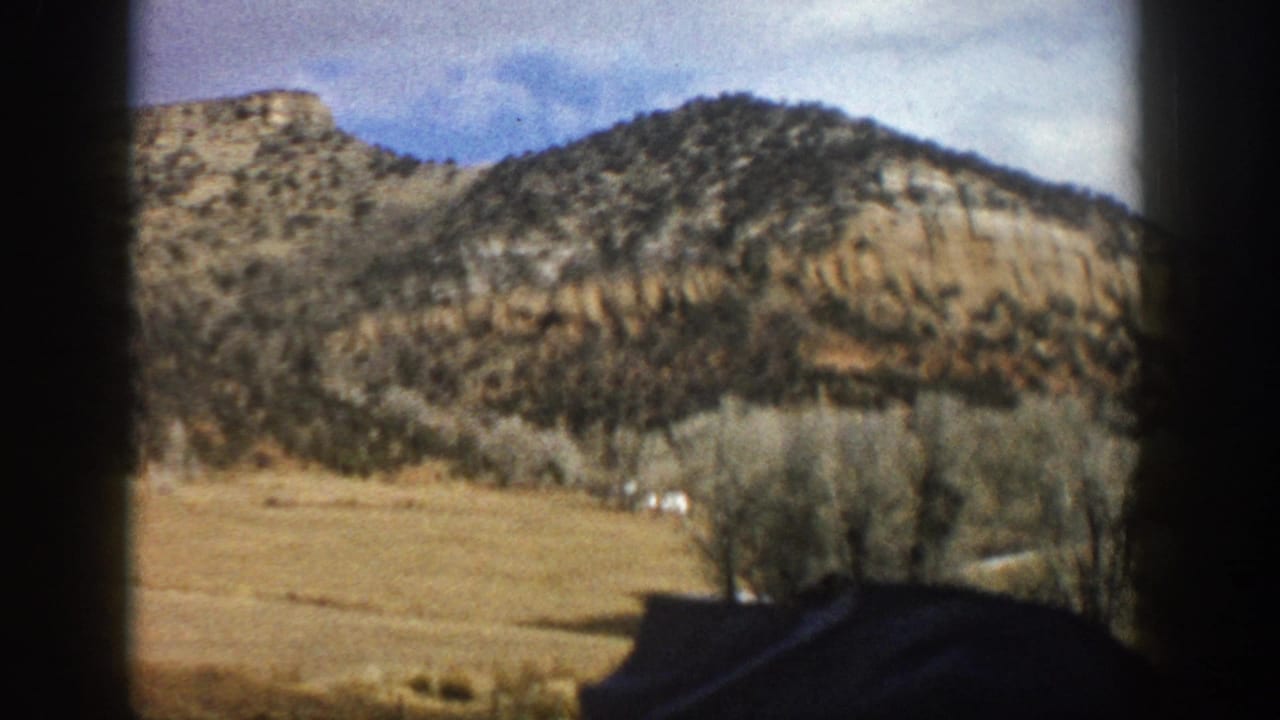 1961 Aspen, Colorado home-movie frame showing rocky hills, dry grass, bare trees, and dark window framing from a moving vehicle.