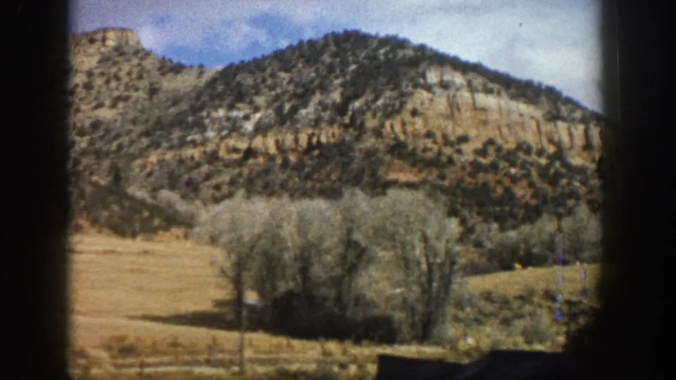 Aspen, Colorado travel footage frame with a tree-dotted rocky slope, open dry field, bare trees, and blue sky in 1961 metadata context.