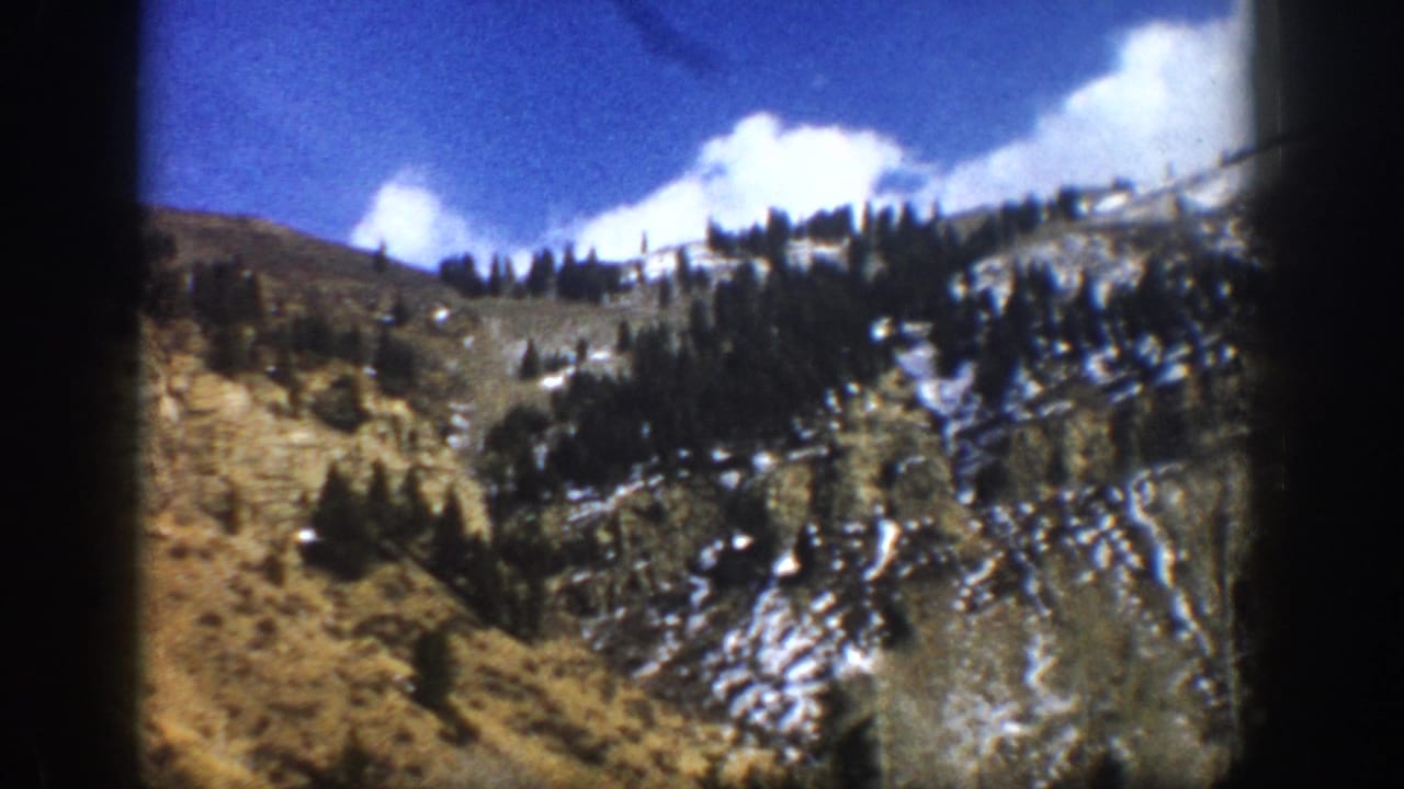 Snow-patched hillside with evergreen trees and clouds above.