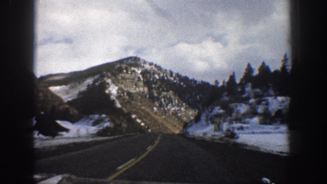 Mountain highway bends through snowy roadside slopes and evergreen trees.