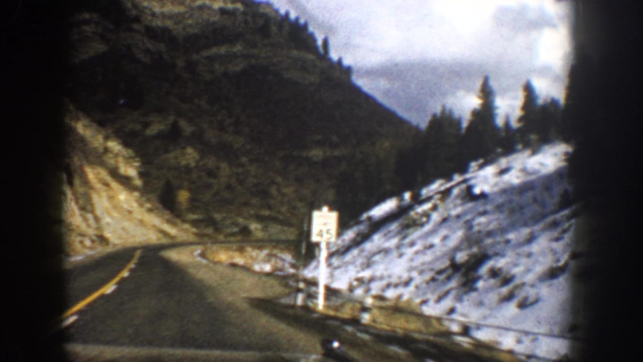 Mountain road curving past a roadside 45 mph sign and snowy hillside.