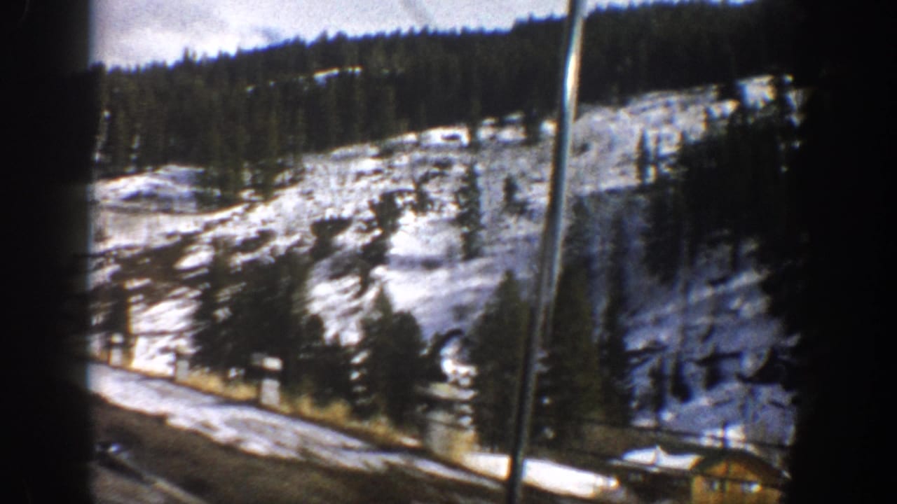 Snowy mountain roadside with evergreen slopes and a small structure near the road.