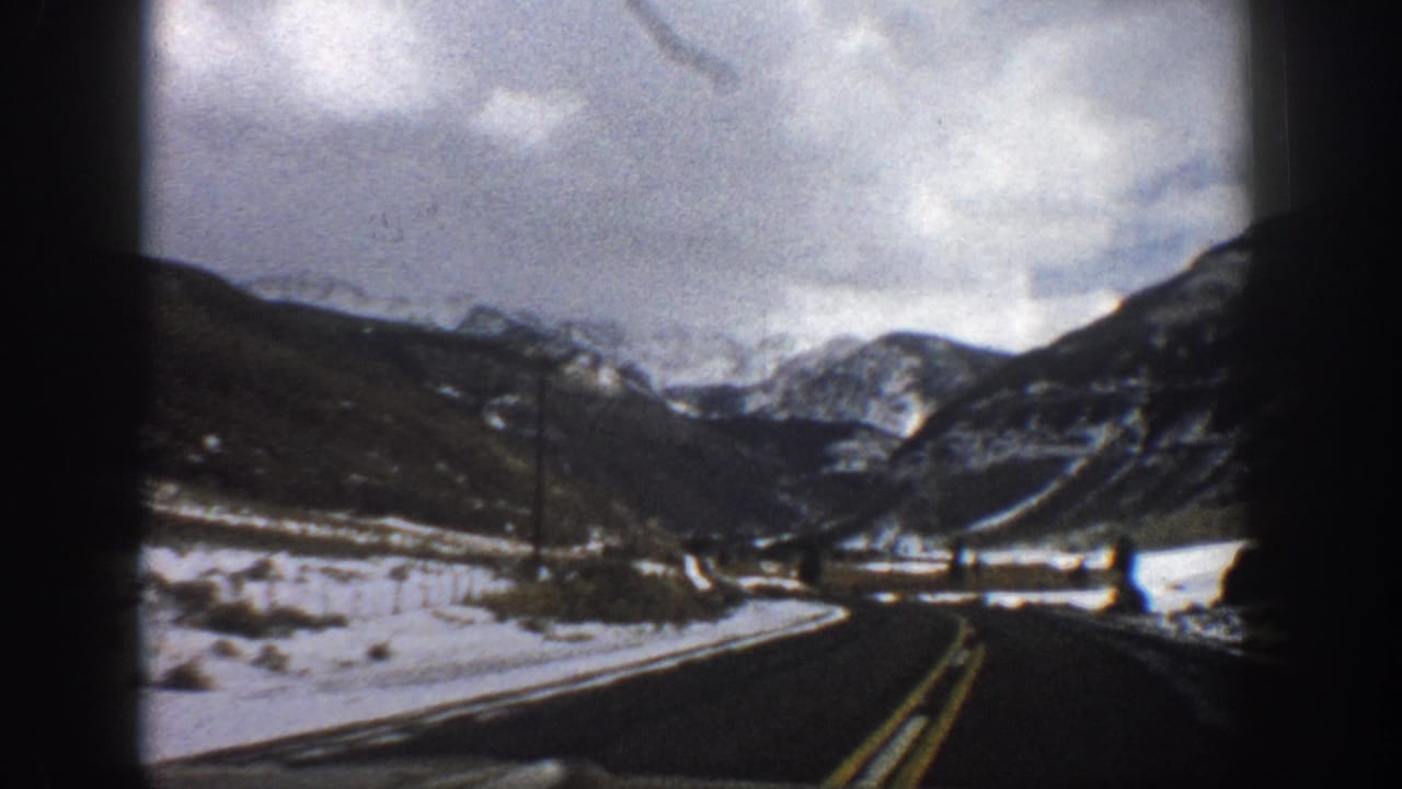 1961 Aspen-area 8mm view from a moving vehicle on a snowy mountain road with telephone poles and distant peaks.