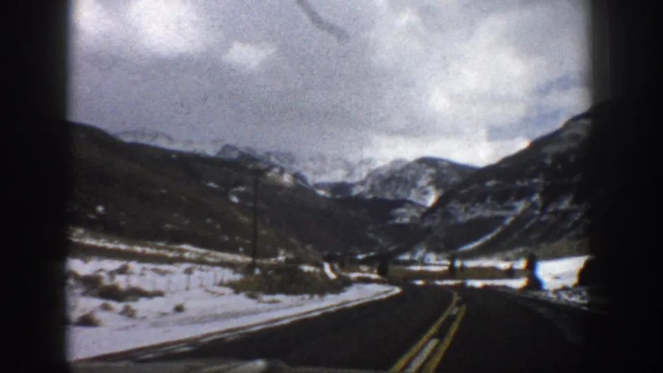1961 Aspen-area 8mm view from a moving vehicle on a snowy mountain road with telephone poles and distant peaks.