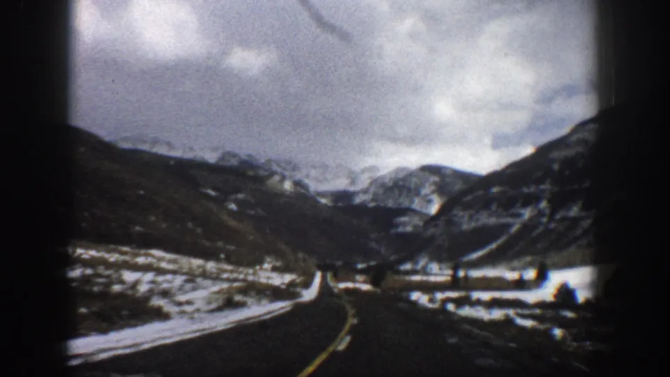 Aspen, Colorado home-movie frame from 1961 showing a moving-car view down a snowy road between mountain slopes.