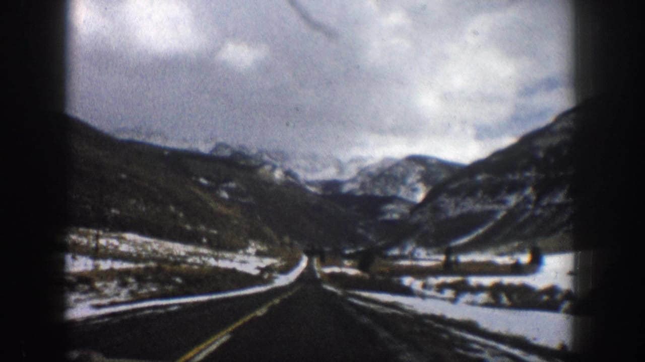 1961 Aspen-area 8mm frame showing a road curving through a snow-dusted mountain valley under heavy clouds.
