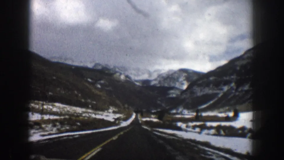 1961 Aspen-area 8mm frame showing a road curving through a snow-dusted mountain valley under heavy clouds.