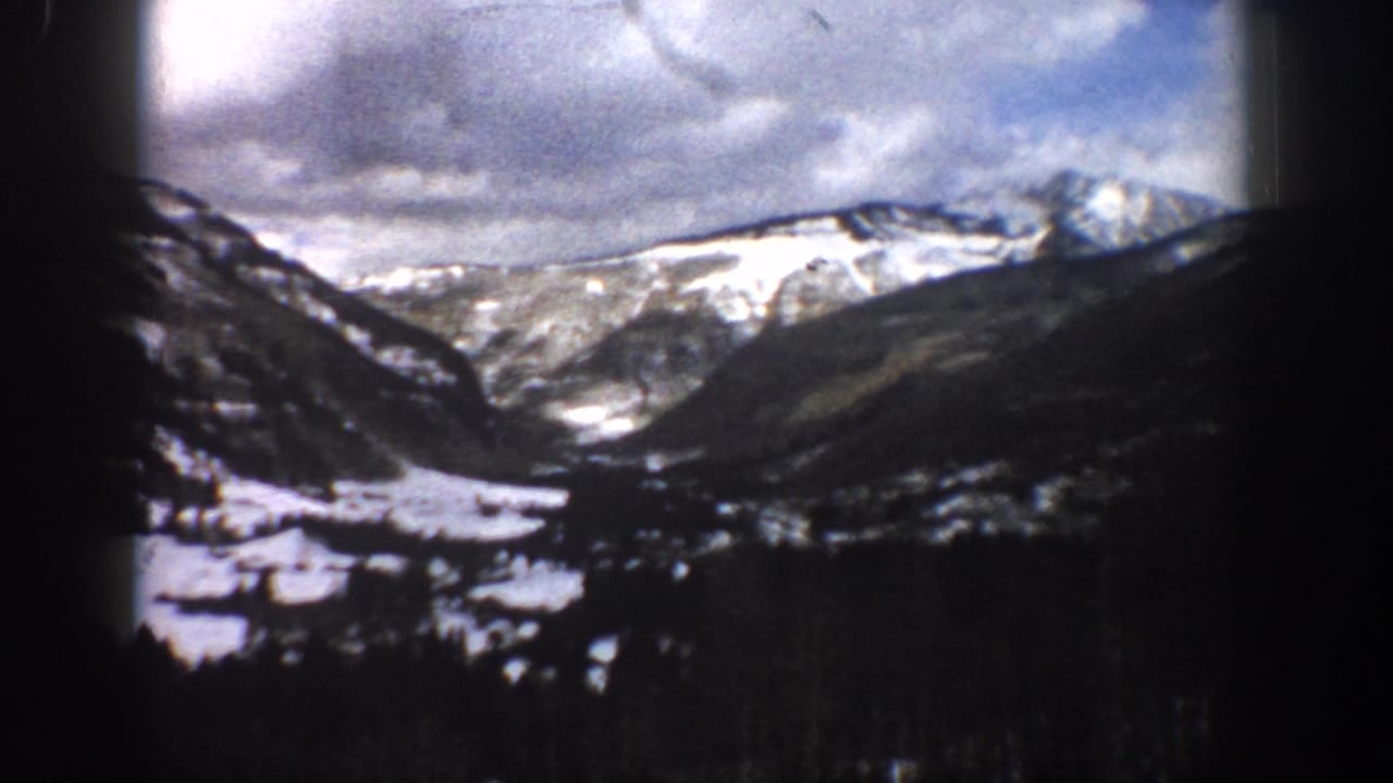 1961 Aspen-area 8mm frame looking across a snowy valley toward rugged mountain ridges beneath a cloudy sky.