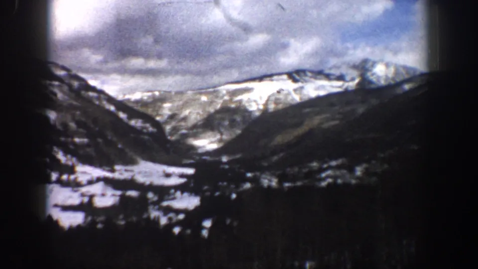 1961 Aspen-area 8mm frame looking across a snowy valley toward rugged mountain ridges beneath a cloudy sky.