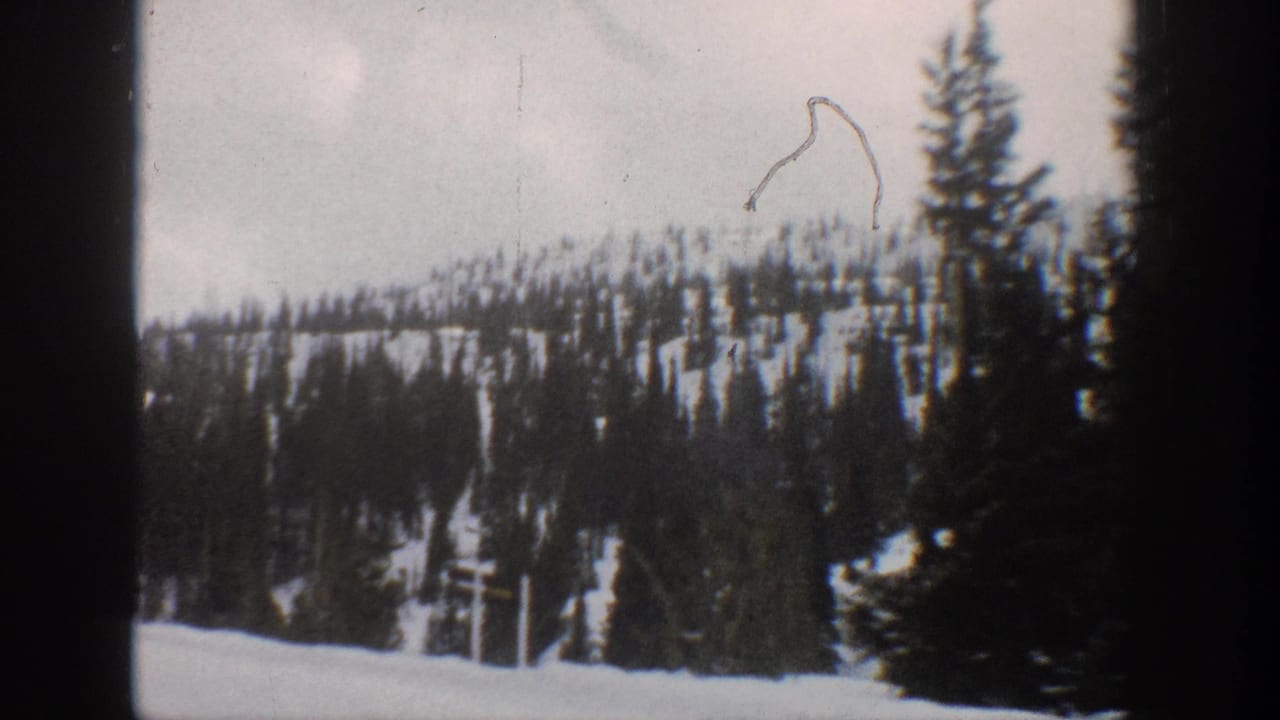 1961 Aspen-area home-movie frame with dark conifers, snowy hillside, pale sky, and visible film wear.