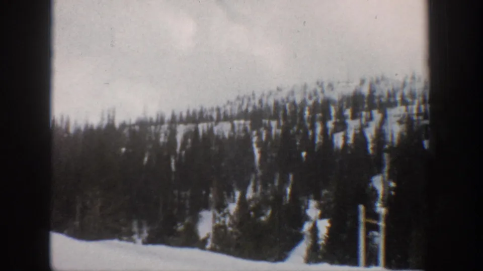 1961 Aspen-area 8mm view of snow-covered ground, conifers, and a forested slope from a moving winter route.
