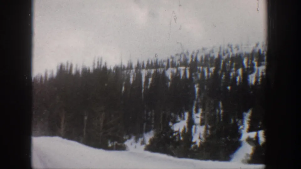 Final 1961 Aspen-area frame showing snowbanks, clustered evergreens, a wooded ridge, and visible 8mm film artifacts.
