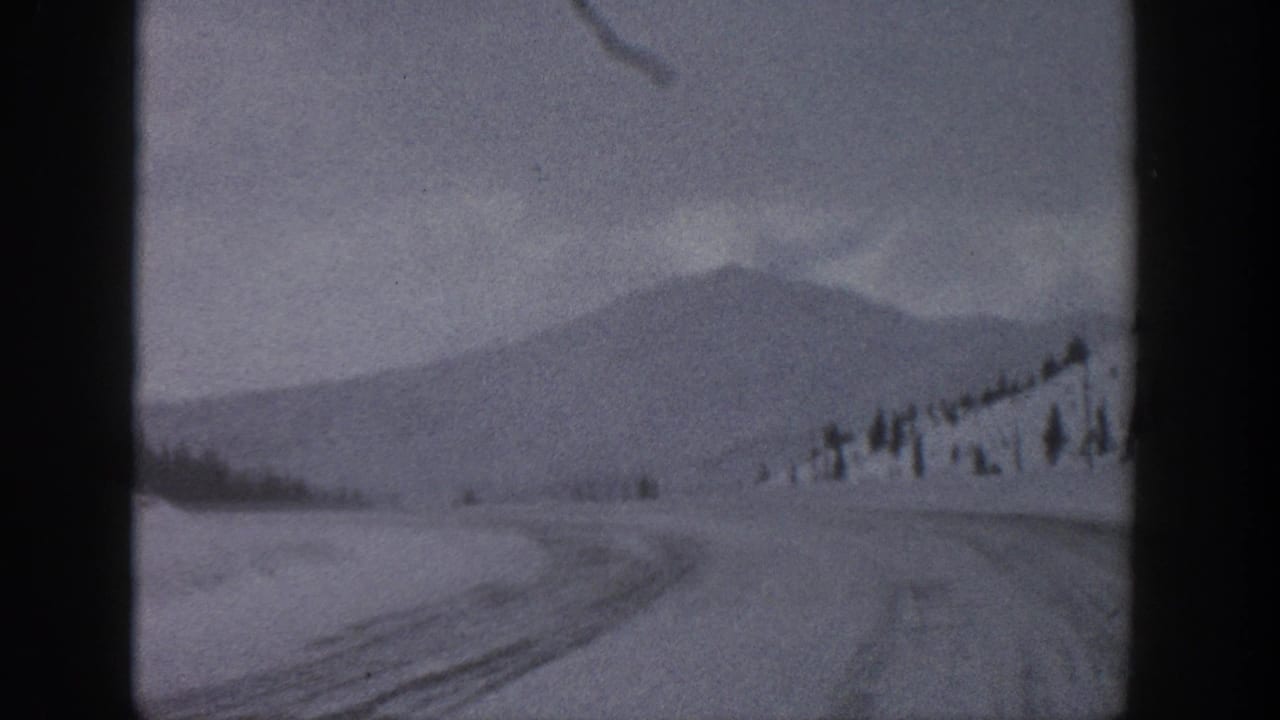 1961 Aspen, Colorado 8mm frame showing a snowy rural road, low mountain slope, scattered evergreens, and overcast sky.