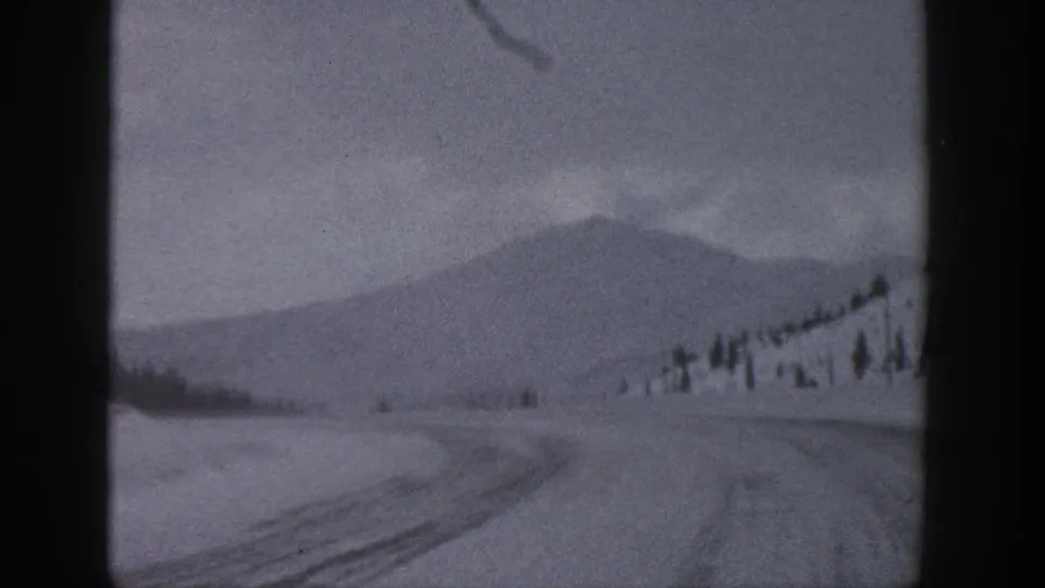 1961 Aspen, Colorado 8mm frame showing a snowy rural road, low mountain slope, scattered evergreens, and overcast sky.