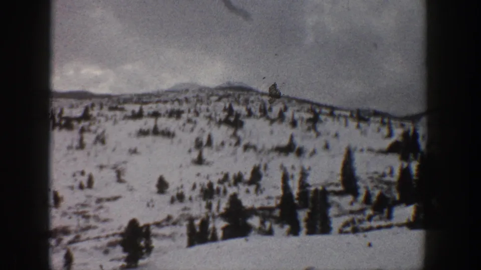 1961 Aspen, Colorado home-movie view of a broad snow-covered hillside, scattered trees, distant mountains, and visible film wear.