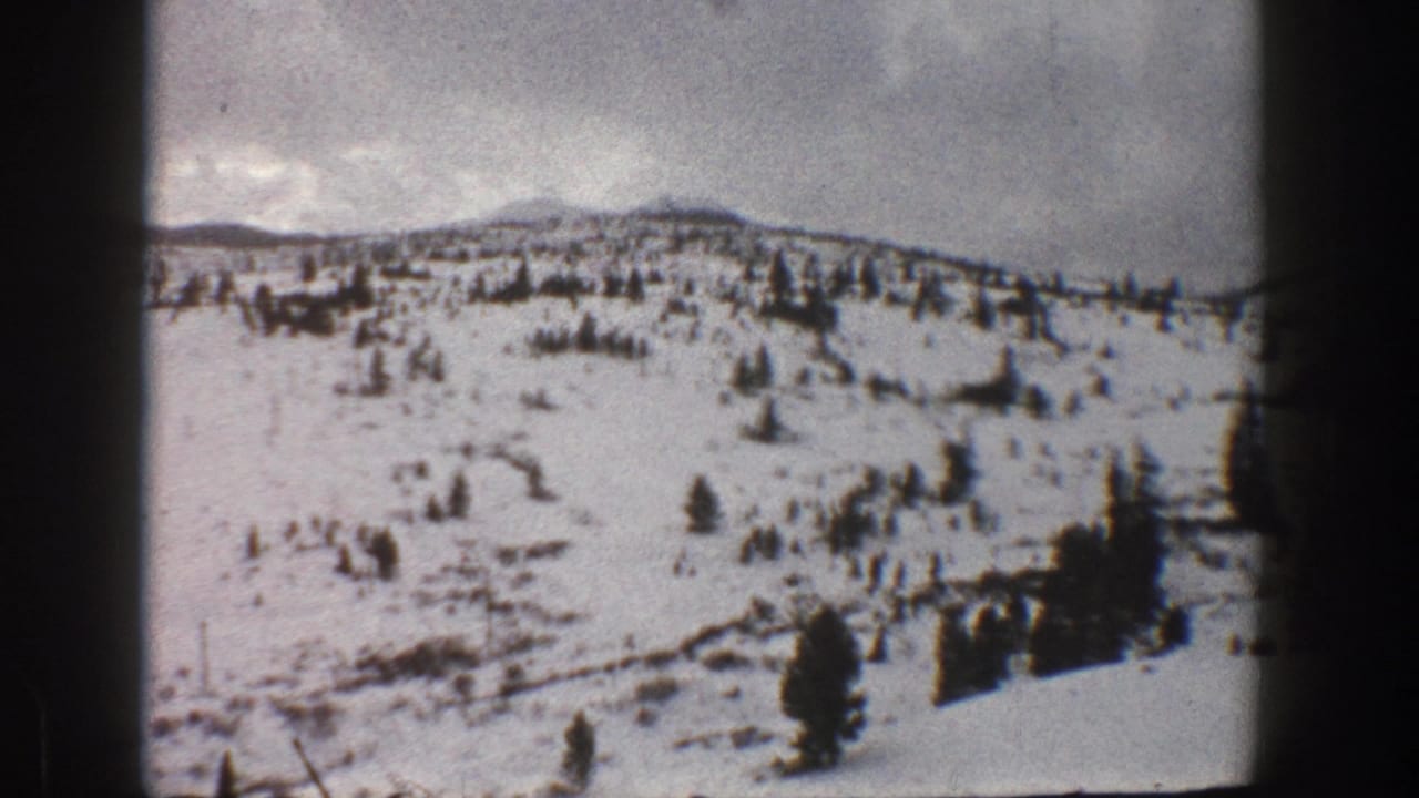 1961 Aspen-area 8mm frame showing a snow-covered hillside with sparse evergreens and dark film edges.