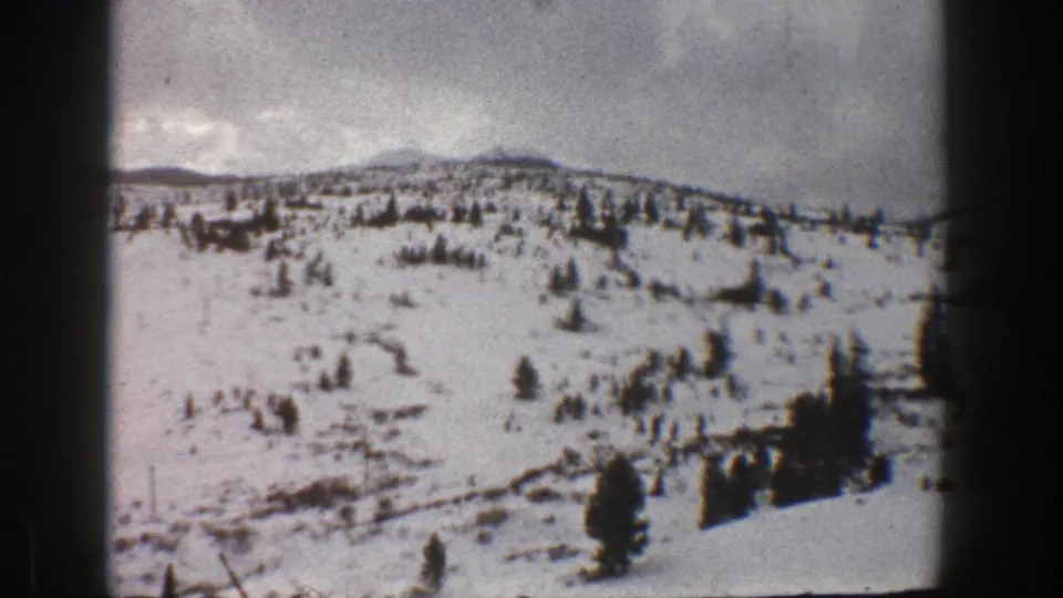 1961 Aspen-area 8mm frame showing a snow-covered hillside with sparse evergreens and dark film edges.