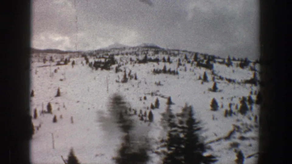 1961 Aspen-area 8mm frame showing a broad snowfield, scattered evergreens, and motion blur from a vehicle viewpoint.