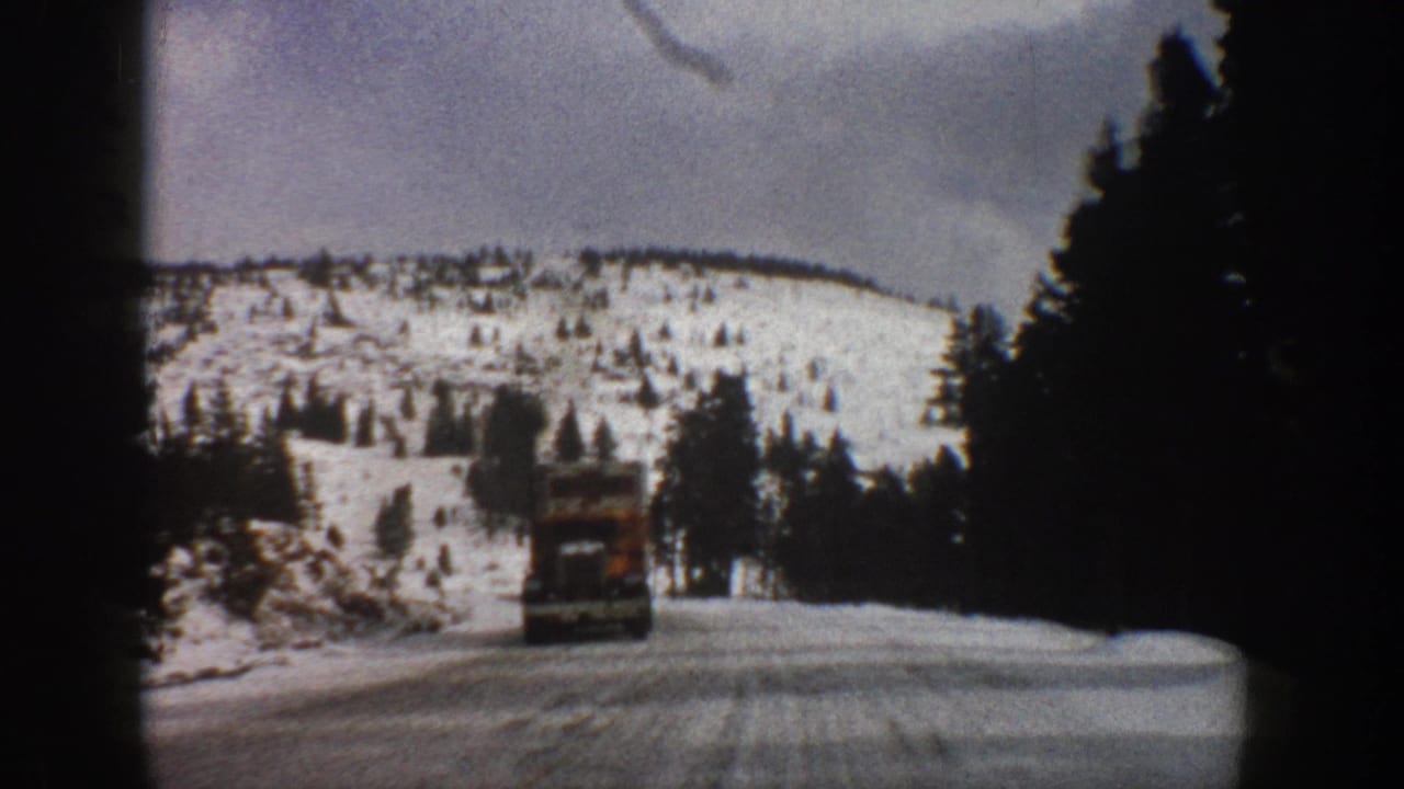 1961 Aspen, Colorado 8mm frame showing a truck traveling ahead on a snowy two-lane mountain road bordered by dark conifers.