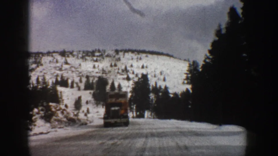 1961 Aspen, Colorado 8mm frame showing a truck traveling ahead on a snowy two-lane mountain road bordered by dark conifers.