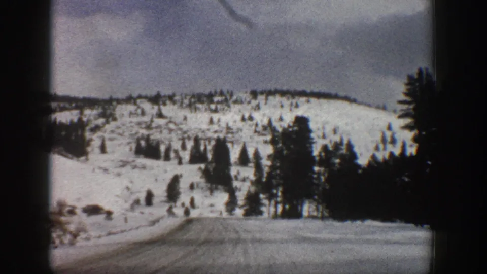 1961 Aspen, Colorado 8mm view of a snow-covered road leading toward a forested hillside after the truck has passed.