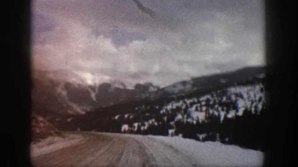 1961 Aspen-area 8mm frame showing a curving snowy road, dark evergreens, and distant winter mountains.