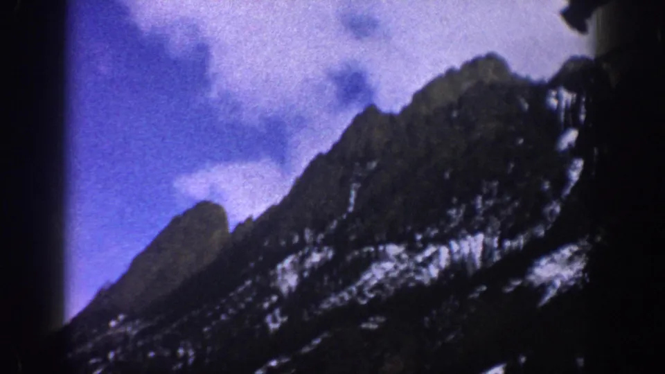 Aspen, Colorado winter home-movie frame showing a steep wooded mountain slope with snow patches and heavy 8mm grain.