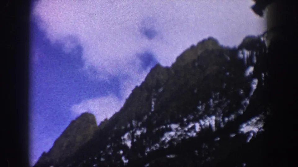 1961 Aspen, Colorado frame of a snow-dusted mountain ridge under cloudy sky, with visible 8mm frame-edge shadow.