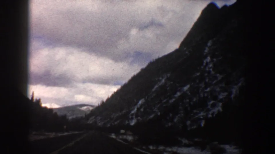 Forward-facing 8mm view near Aspen in 1961, showing a road curving through a cloudy, snow-dusted mountain valley.