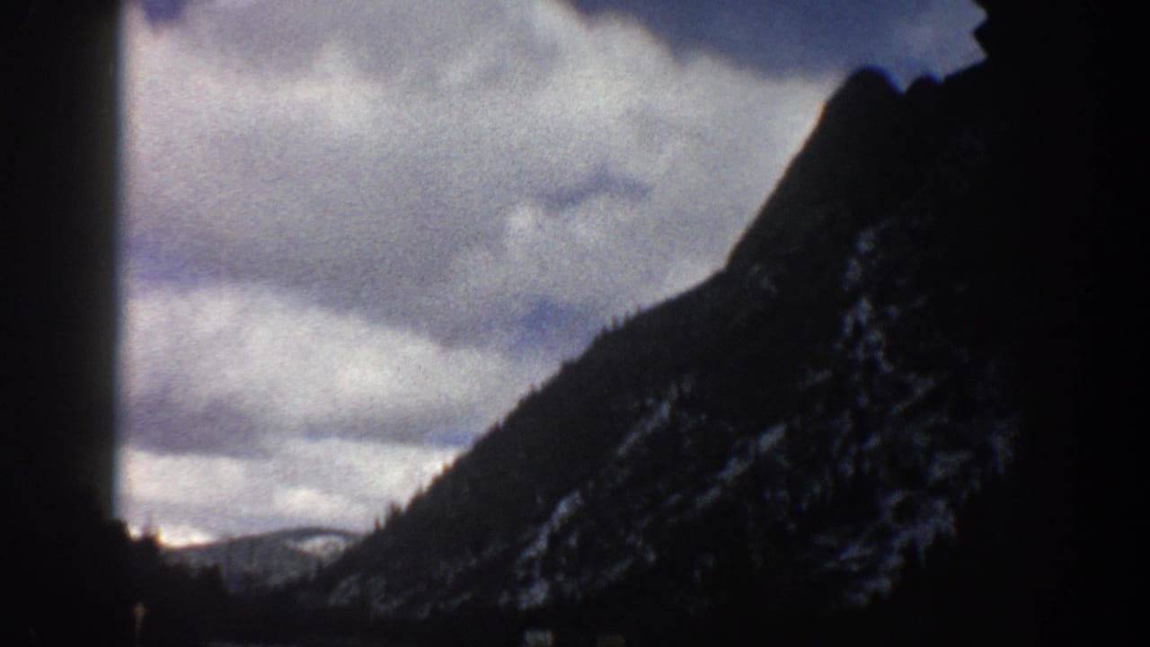 Dark car-window framing around a steep mountain slope beneath cloudy sky.