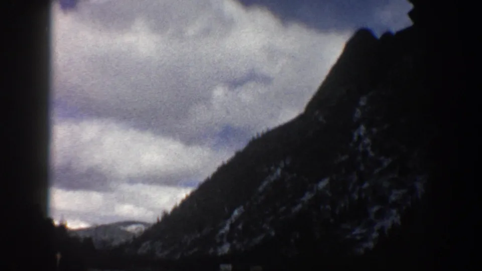1961 Aspen, Colorado home-movie frame showing a steep mountain slope and clouds through a dark vehicle interior frame.