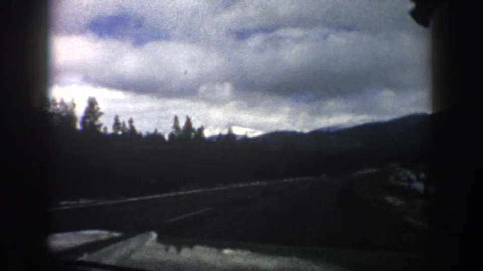 Aspen, Colorado home-movie frame with the car looking ahead toward trees, snow along the road, and low mountain ridges.