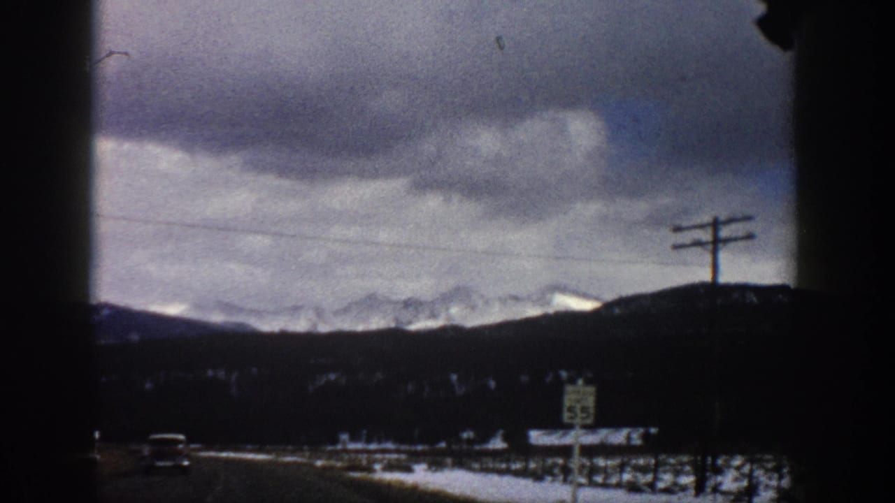 Aspen, Colorado winter roadside scene from 1961, showing snowy fields, a speed limit sign, utility poles, and distant mountain ridges.