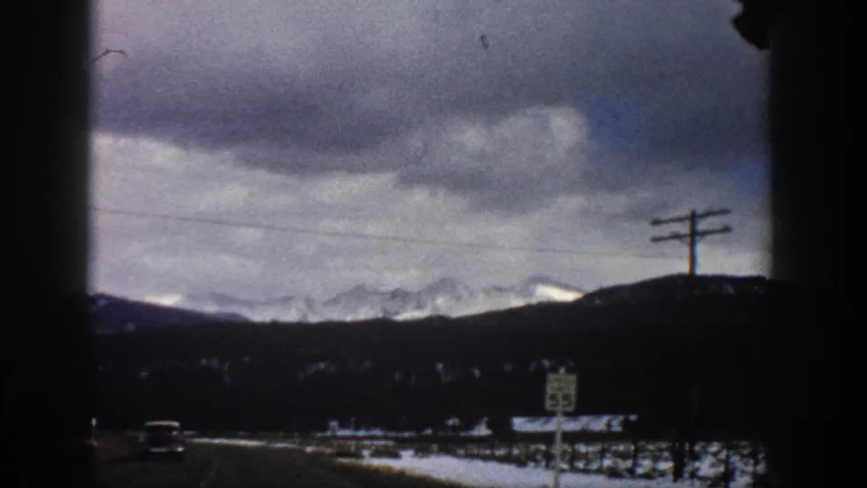 Aspen, Colorado winter roadside scene from 1961, showing snowy fields, a speed limit sign, utility poles, and distant mountain ridges.