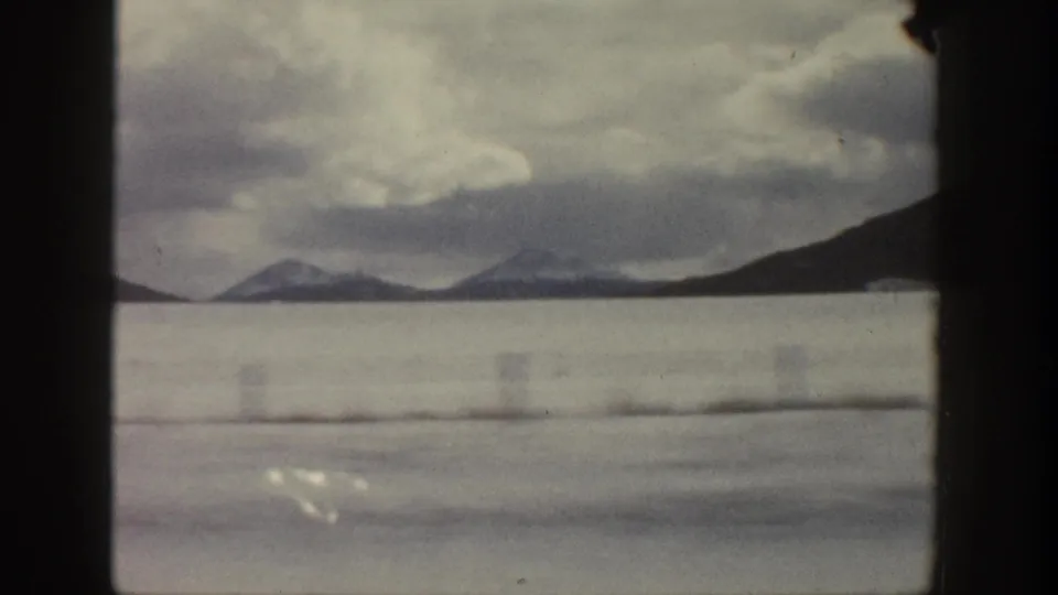1961 Aspen winter field view with broad snow cover, distant mountain slopes, low clouds, and visible 8mm frame edges.
