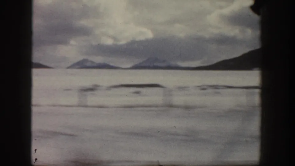Aspen-area 8mm winter view from 1961, with a pale snowfield, distant mountains, cloudy sky, and dark film-frame borders.